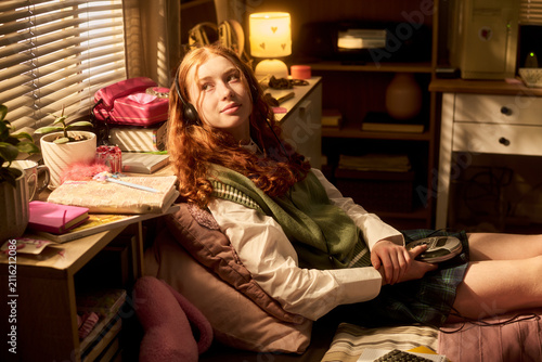 Teenage Caucasian girl wearing headphones  reclining beside desk and listening to portable CD player at home  expressing nostalgia and youth culture. Ideal for retro lifestyle marketing