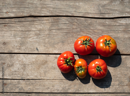 Fresh ripe red tomatoes grouped on a weathered rustic wooden table in bright natural sunlight. Top view flat lay composition with deep shadows and ample copy space