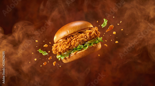 Crispy fried chicken sandwich floating in midair with flying lettuce and crumbs on a smoky background