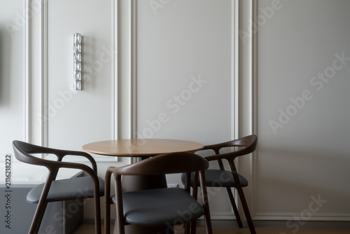 Contemporary dining set featuring a round wooden table and sculpted chairs with dark gray cushions, creating a stylish and functional interior space against a paneled wall