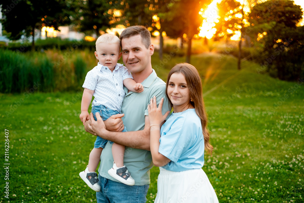 Fototapeta premium parents, mom, dad, and a small child are walking on a green lawn in the summer, having fun together, hugging, and playing outside in the summer. A happy family