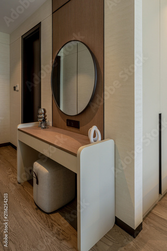 Modern dressing table interior with a round mirror and soft square stool in a luxury home.