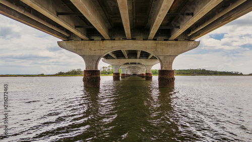 View of bridge supports over calm water on a cloudy day in a coastal area