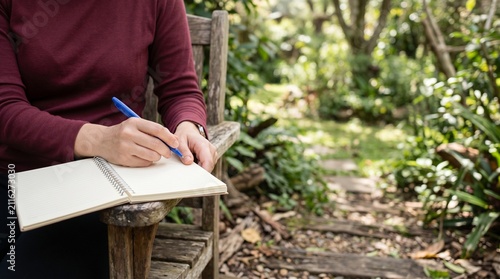 A contemplative individual sitting on a weathered garden bench while carefully writing notes in a spiral notebook amidst a peaceful lush forest