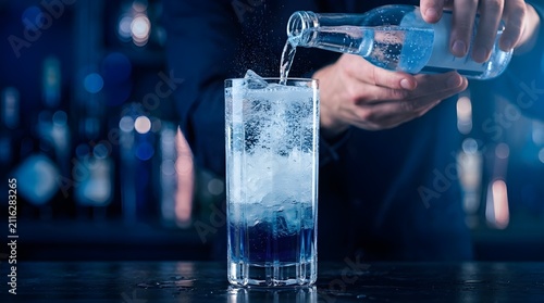 Bartender pouring sparkling tonic into a tall glass filled with ice and blue layered liquid