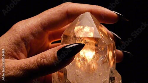 Close up of a hand with black nails holding a glowing citrine crystal against a dark background