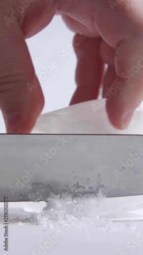 A hand holds a knife and slices steadily across a white block of ice in close-up, scraping thin shavings downward and sideways, creating a satisfying ASMR texture and sound.