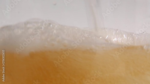 Golden beer pours steadily into a glass in close-up, forming thick white foam on top as bubbles rise through the liquid, creating a satisfying ASMR pouring sound and texture.