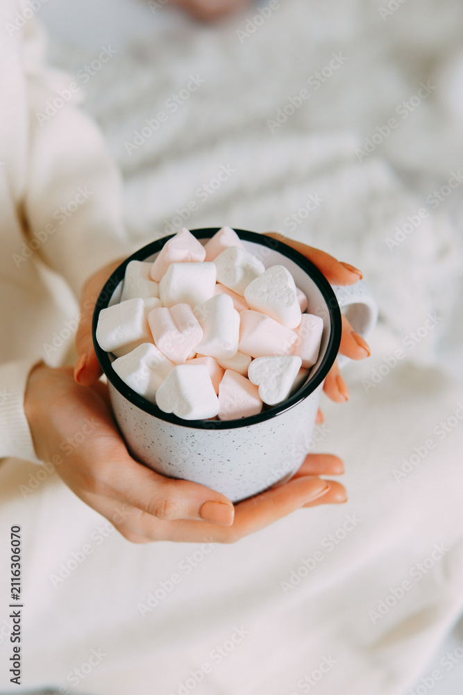 Obraz premium Woman holding white cup filled with heart shaped marshmallows. Cozy comfort atmosphere during Christmas holiday season. Delicious sweet hot drink for winter relaxation and love celebration.