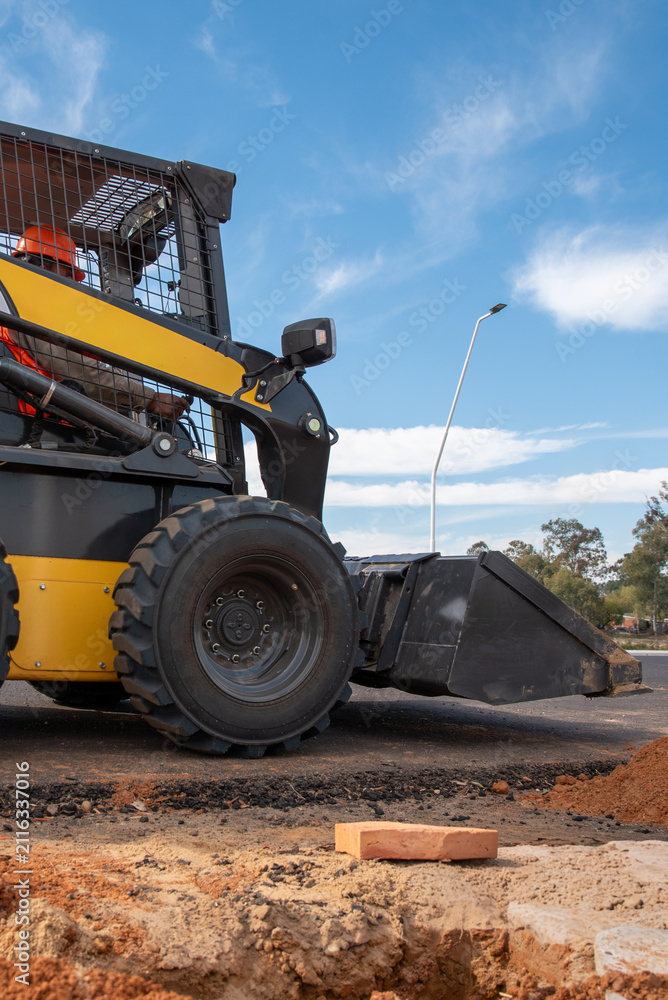 Fototapeta premium Skid steer loader operating on new asphalt road under clear sky