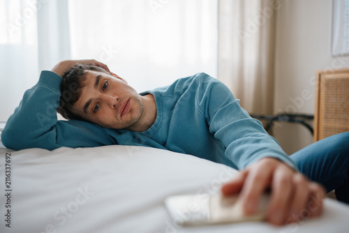 Man lying on bed checking phone after breakup