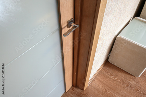 interior shot features a light‑wood interior door with a sleek metal handle, set against white paneled walls, beige textured wallcovering, and warm wood‑look flooring