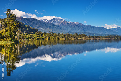 Beautiful lake Ianthe at the bottom of Southern Alps on The West Coast of South Island in New Zealand, mountains, forest, blue sky with reflection