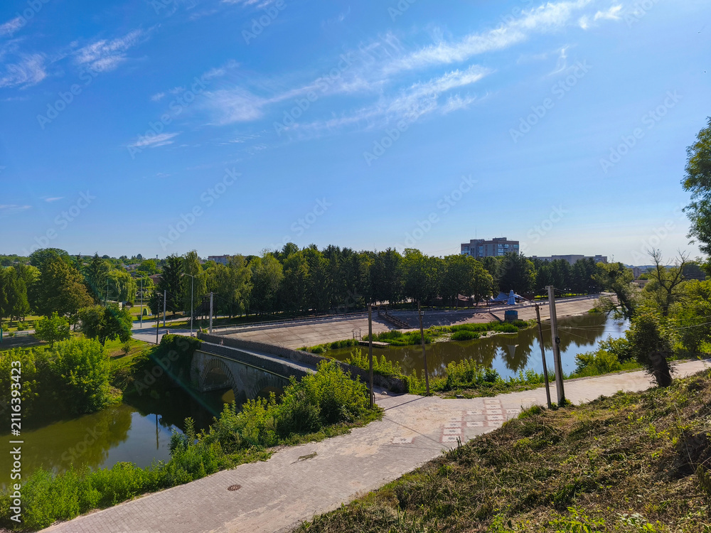 Fototapeta premium Scenic View Of River With Bridge Surrounded By Green Trees And Sky
