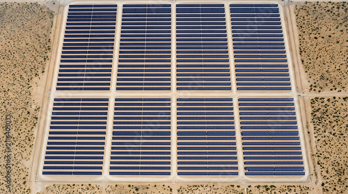Vast Solar Array in Desert Landscape: An expansive solar farm stretches across a dry, arid desert landscape, its rows of photovoltaic panels glistening under a clear sky.