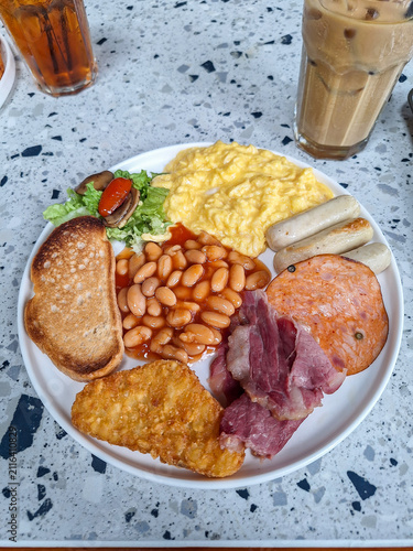 Canvastavla Close-up of a traditional full English breakfast plate featuring scrambled eggs, baked beans, sausages, toast, and a hash brown on a terrazzo table