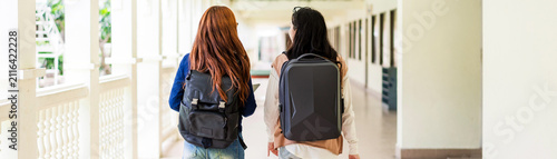 Two students with backpacks walk down a bright campus corridor toward class.