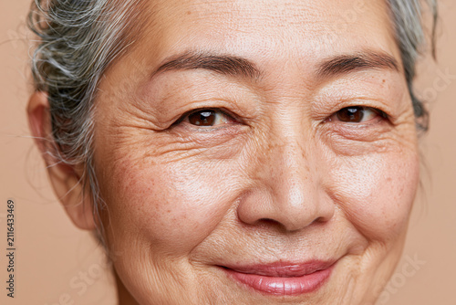 Elderly Asian woman close up portrait showing detailed skin texture, smile lines, gray hair and warm expression, natural light highlighting facial features and freckles