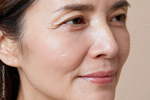 Close up mature Asian woman skin texture with natural glow, visible wrinkles and pores, gentle expression conveying confidence and calm skincare concept