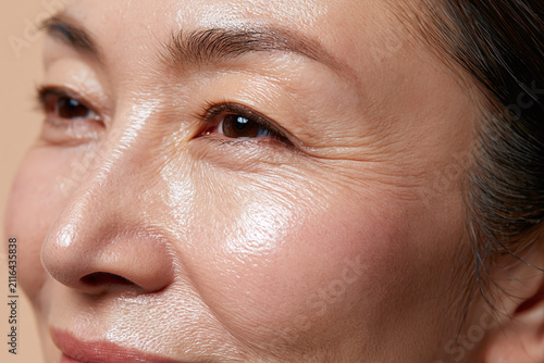 Radiant middle aged Japanese woman closeup showing smooth skin texture, fine wrinkles and natural makeup, glowing cheek and eye area conveying confidence and warmth