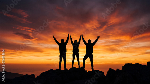 Silhouetted Hikers Standing on High Mountain Cliff Cheering at Bright Sunrise