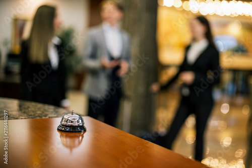 Close-up of a hotel bell on a luxury reception desk with people in background