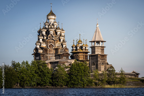 View of the historic wooden Kizhi Pogost church with its iconic multiple domes, surrounded by lush green trees on the shore of Lake Onega in Petrozavodsk, Republic of Karelia, Russia.