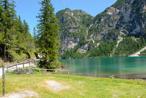 Scenic view of Lake Braies (Pragser Wildsee) with turquoise water, alpine mountains, evergreen forest and cycling trail on a sunny summer day in the Italian Dolomites.