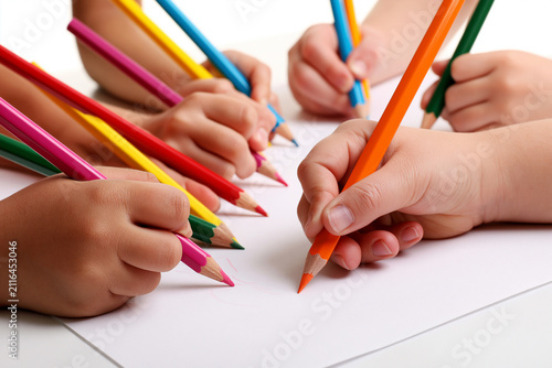 Gros plan sur des mains d'enfants d'origines diverses dessinant ensemble avec des crayons de couleur sur une grande feuille, isolées sur fond blanc