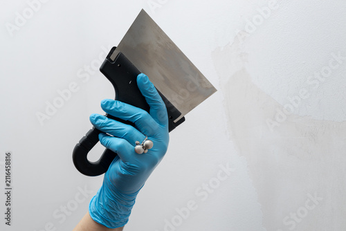 Fotografía Hand in blue glove scraping paint off the wall with putty knife