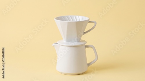 Modern white ceramic pour-over coffee dripper set with server pitcher, isolated on a clean light yellow pastel background.