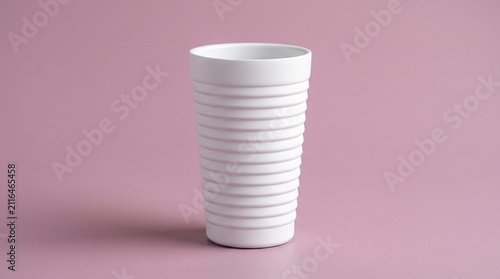 White ceramic tumbler with textured horizontal ridges isolated on a dusty pink background. Minimalist drinkware perfect for modern kitchenware or tableware design.