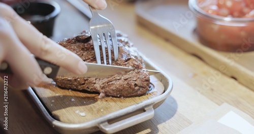 Hands cutting grilled steak on wooden board