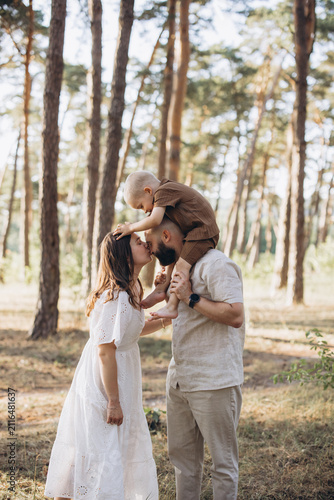 Happy family with young son on father s shoulders  parents kissing during summer walk in a green forest