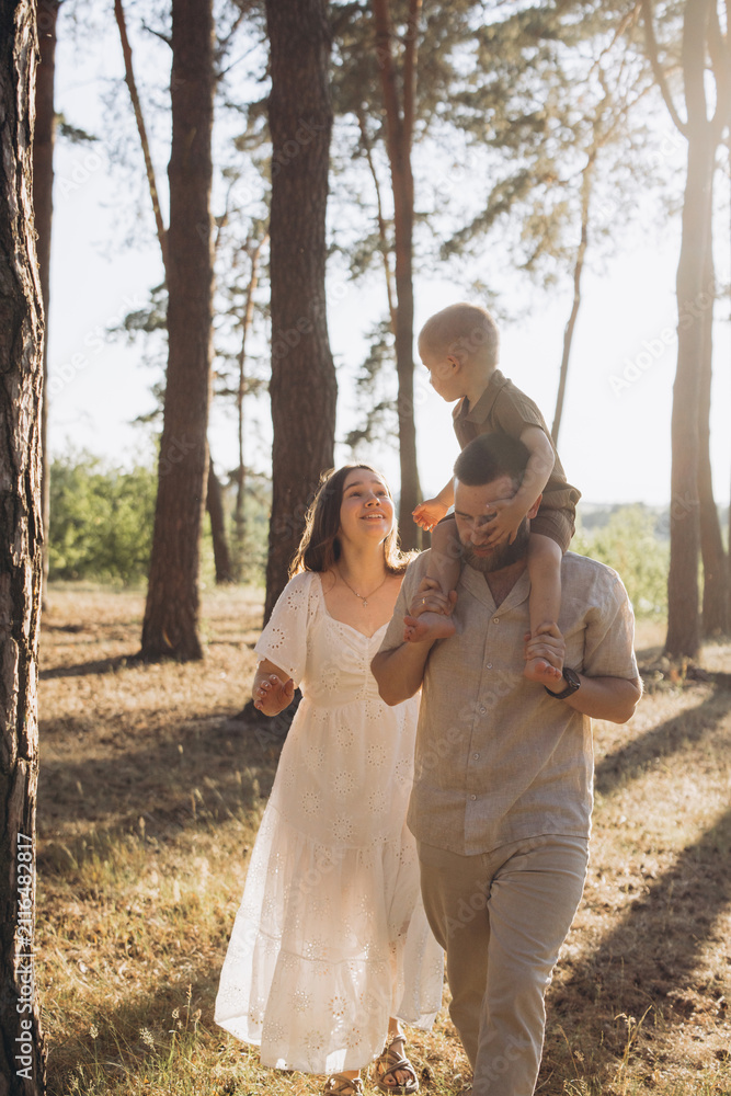 Obraz premium Happy family with child on shoulders walking in summer forest during golden hour, enjoying leisure time outdoors