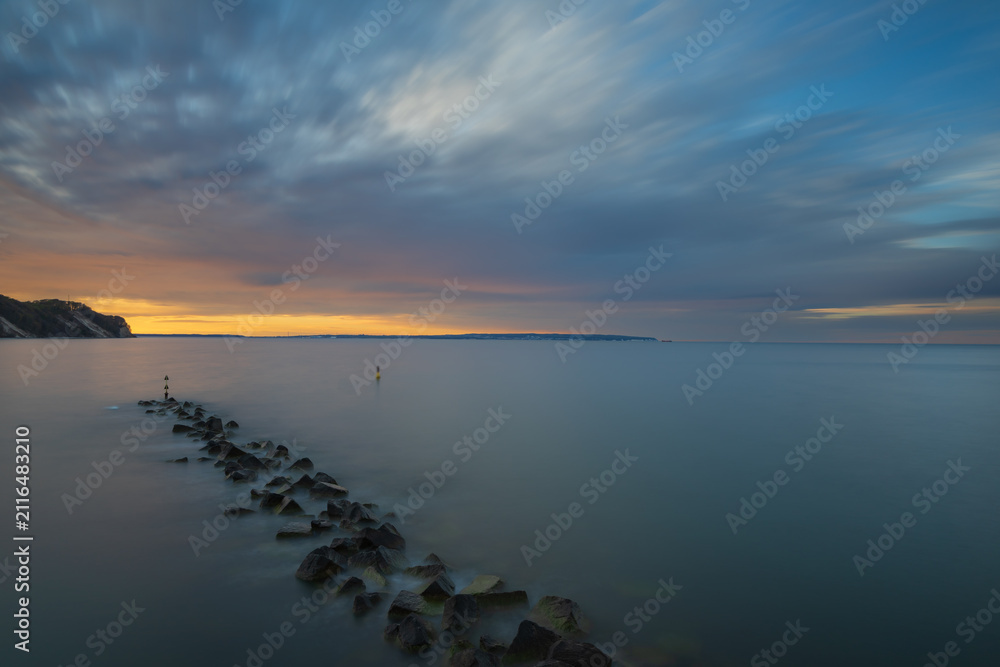 Fototapeta premium Rock breakwater stretching into smooth calm sea under vibrant sunset sky during twilight