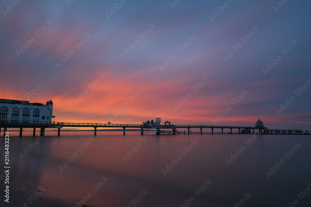 Obraz premium Historic Sellin pier resort building and walkway silhouetted against glowing orange sunset sky