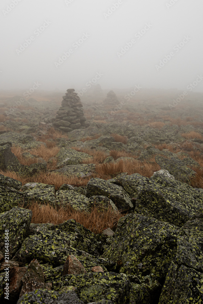 Obraz premium Foggy mountain landscape with rock cairns, navigation and wilderness