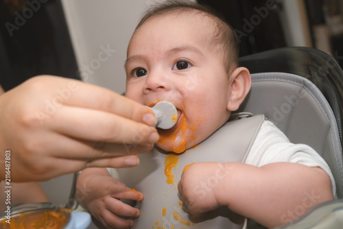Fotografie Bebé niño comiendo papilla de zanahoria en la silla