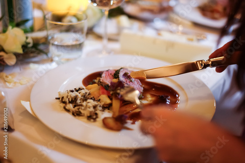 A person is enjoying a meal at a wedding. The plate contains meat, rice, and vegetables. Soft lighting adds to the atmosphere.