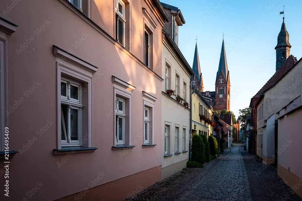 Fototapeta premium Historic cobblestone alley leading to church towers in Neuruppin, Brandenburg, Germany