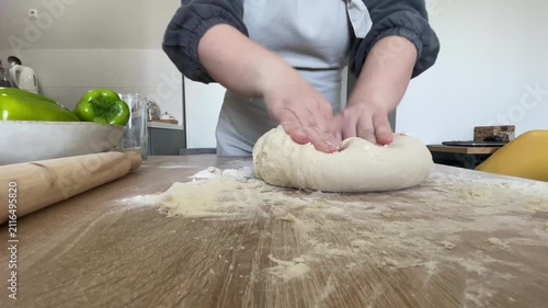 The hands of a female cook knead a lump of dough on a wooden table with white wheat flour.
