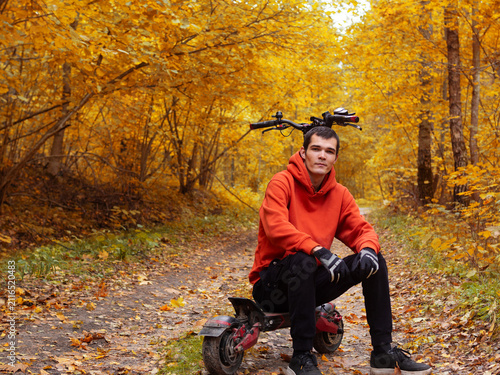 young man on an electric scooter in an autumn forest . Silent electric transport for park rides
