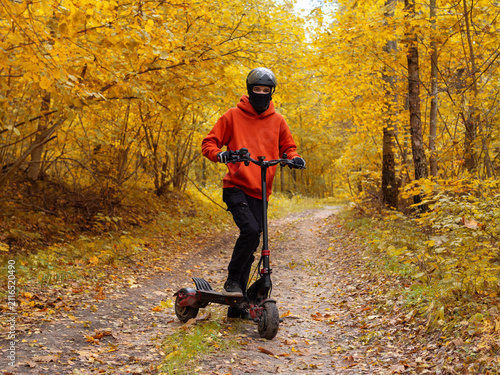 young man rides an electric scooter in an autumn forest