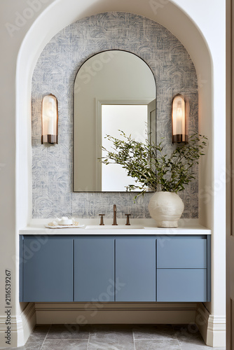 A bathroom vanity featuring dusty blue flat-front floating shelves, an arched mirror, wall lights, and a geometric wall texture, all within a contemporary decor scheme