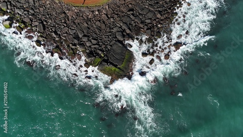Top-down aerial drone view of Atlantic Ocean waves crashing against the volcanic rocky coastline of Saint Joseph Island, one of the Salvation Islands archipelago in French Guiana, South America.