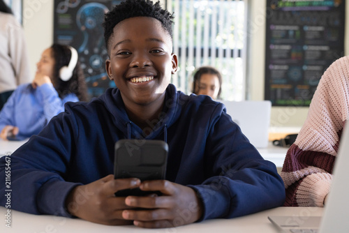 African American students in class, smiling student in navy hoodie holding smartphone, laptops