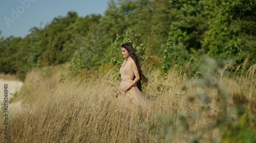 A young woman stands in a sunny meadow, surrounded by tall grass. The concept of enjoying the beauty of nature.