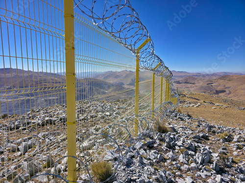 Принти на полотні Yellow metal perimeter fence with concertina wire running along the crest of a h