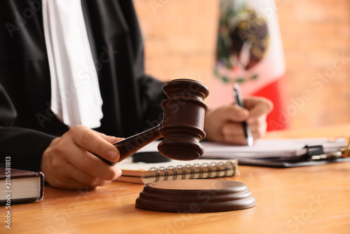 Foto Judge holding a wooden gavel in a courtroom with a Mexican flag in the backgroun